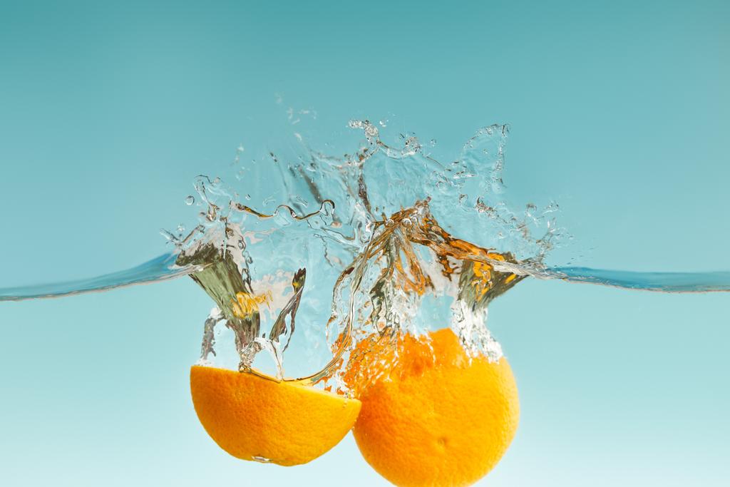 naranja de corte maduro que cae en el agua con salpicaduras sobre fondo azul
 - Foto, imagen