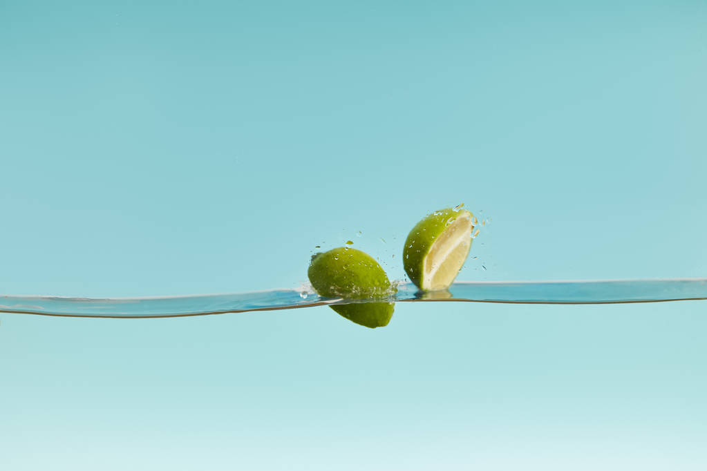 metades de limão maduro caindo na água sobre fundo azul
 - Foto, Imagem