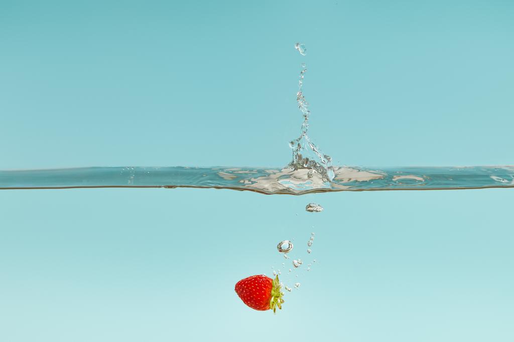 fraise mûre tombant dans l'eau avec éclaboussure sur fond bleu
 - Photo, image