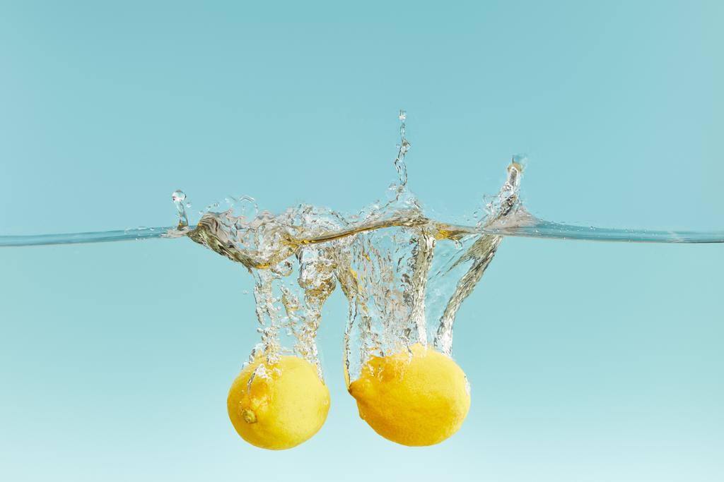ολόκληρα λεμόνια που πέφτουν βαθιά στο νερό με βουτιά σε μπλε φόντο - Φωτογραφία, εικόνα