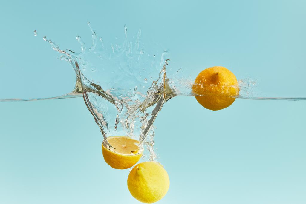 Свежие спелые лимоны падают глубоко в воду с брызгами на синем фоне
 - Фото, изображение