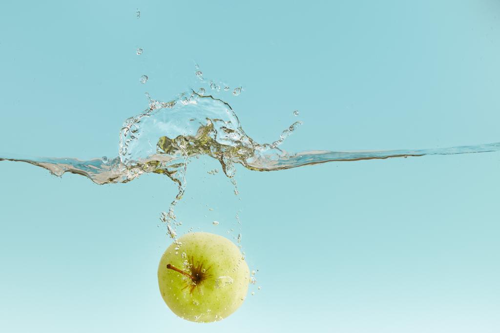 зелене яблуко глибоко падає у воду з бризкою на синьому фоні
 - Фото, зображення