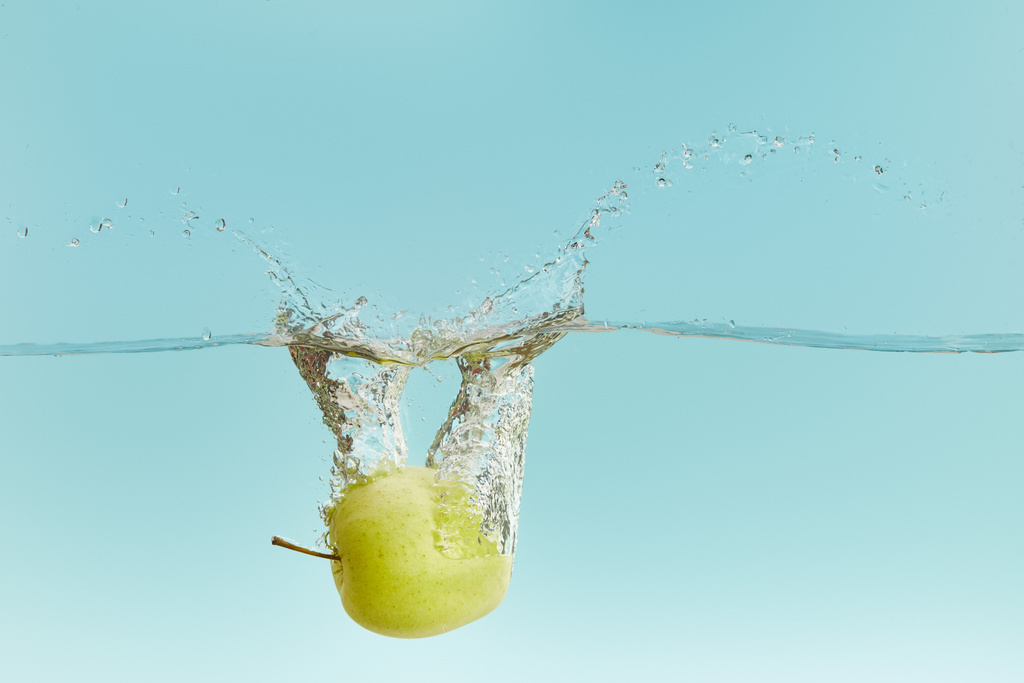 kypsä vihreä omena putoaa syvälle veteen roiskeita sinisellä pohjalla
 - Valokuva, kuva