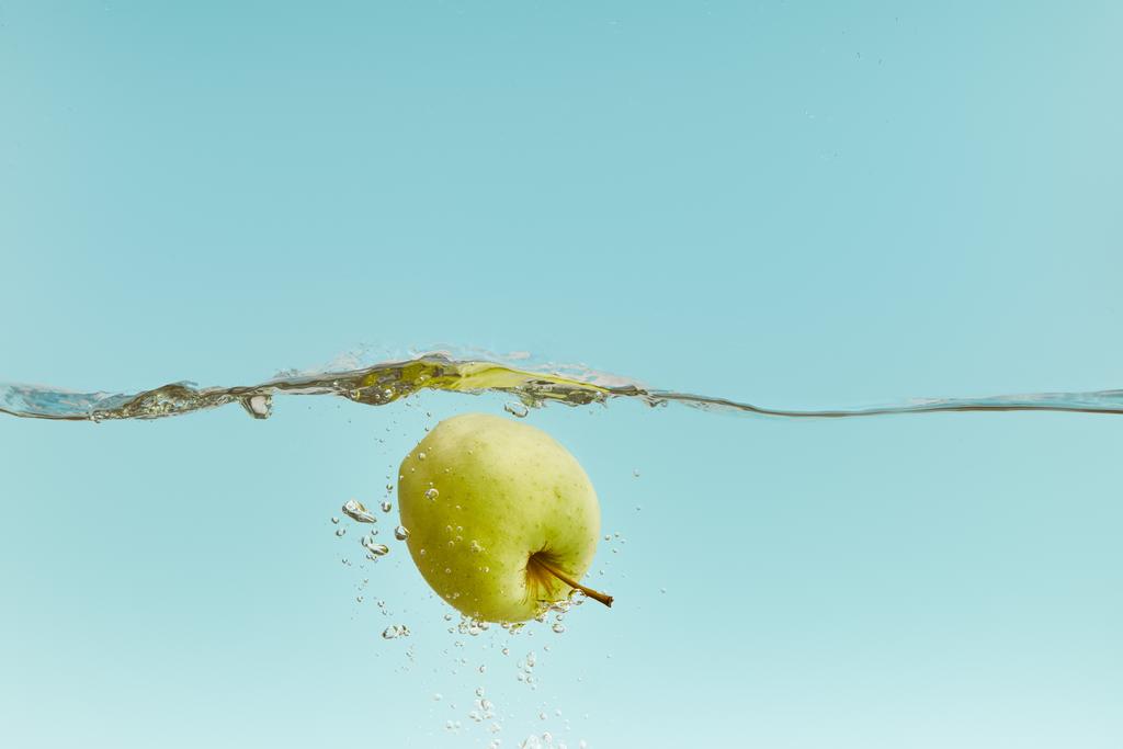 verse groene appel in water met bubbels op blauwe achtergrond - Foto, afbeelding