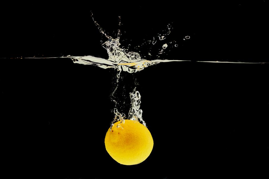 黒に隔離されたスプラッシュで水の深く落ちるレモン - 写真・画像