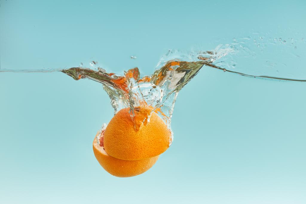 świeże pomarańczowe połówki opadające w wodzie na niebieskim tle - Zdjęcie, obraz