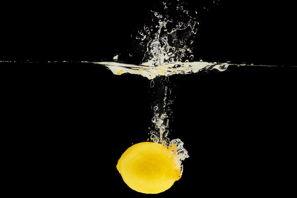 gelbe reife Zitrone fällt tief ins Wasser mit Spritzer isoliert auf schwarz - Foto, Bild