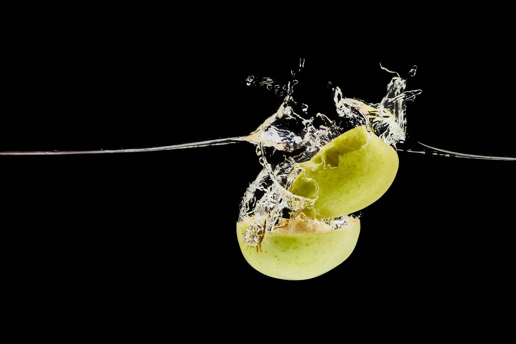 manzana verde cortada que cae profundamente en el agua con salpicadura aislada en negro
 - Foto, Imagen