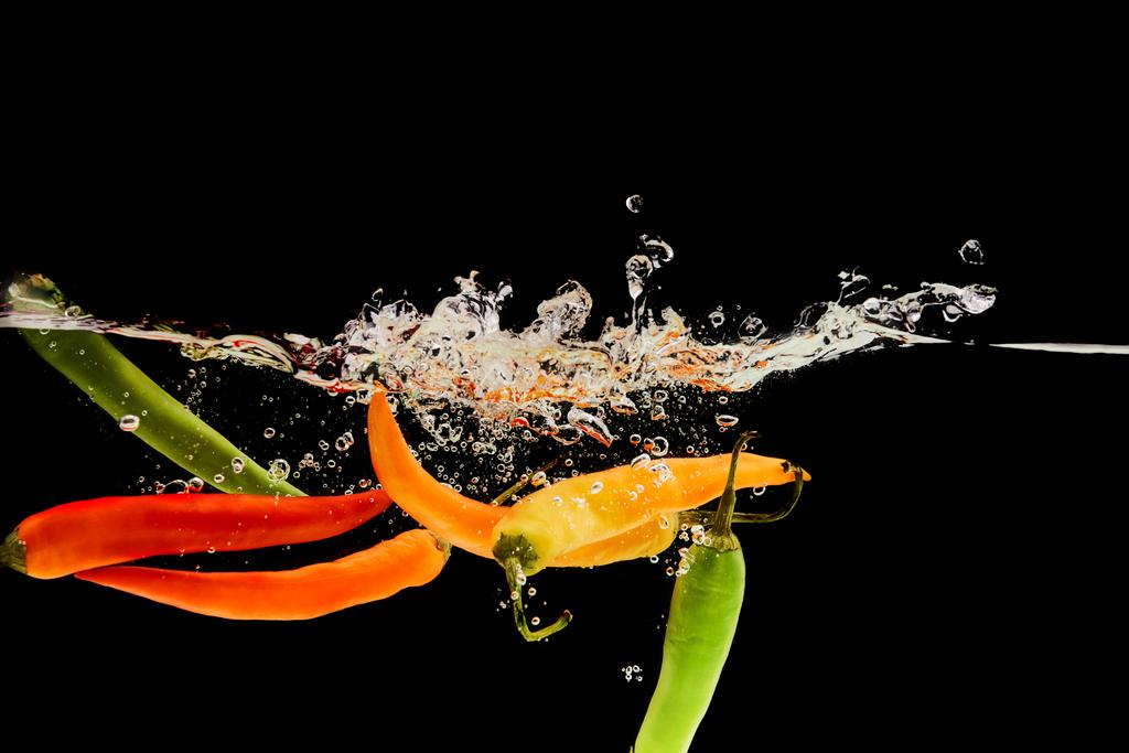 барвистий перець чилі падає глибоко у воді зі сплеском ізольовано на чорному
 - Фото, зображення