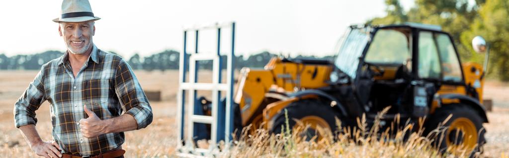 tiro panorámico de granjero barbudo feliz mostrando el pulgar hacia arriba cerca del tractor
  - Foto, imagen