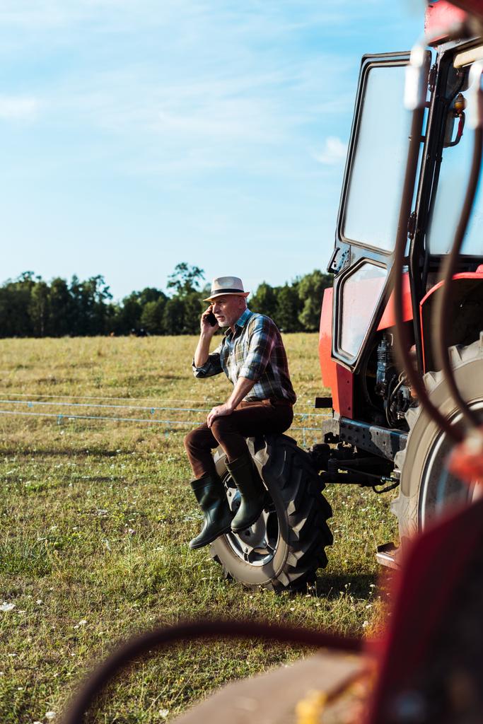 enfoque selectivo de agrónomo barbudo hablando en smartphone cerca del tractor
  - Foto, imagen
