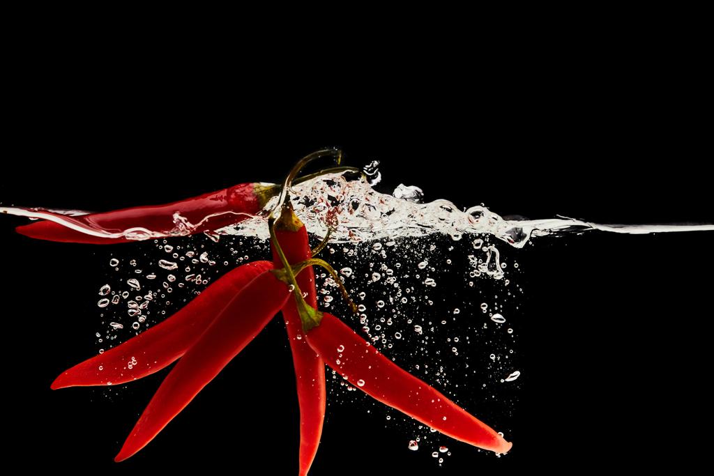 reife rote Chilischoten fallen in Wasser mit Spritzer isoliert auf schwarz - Foto, Bild