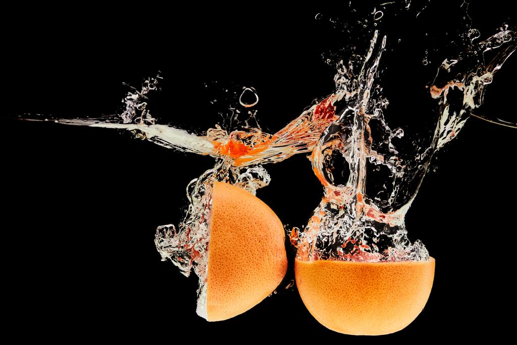 grapefruit halves falling in water with splash isolated on black - Photo, Image