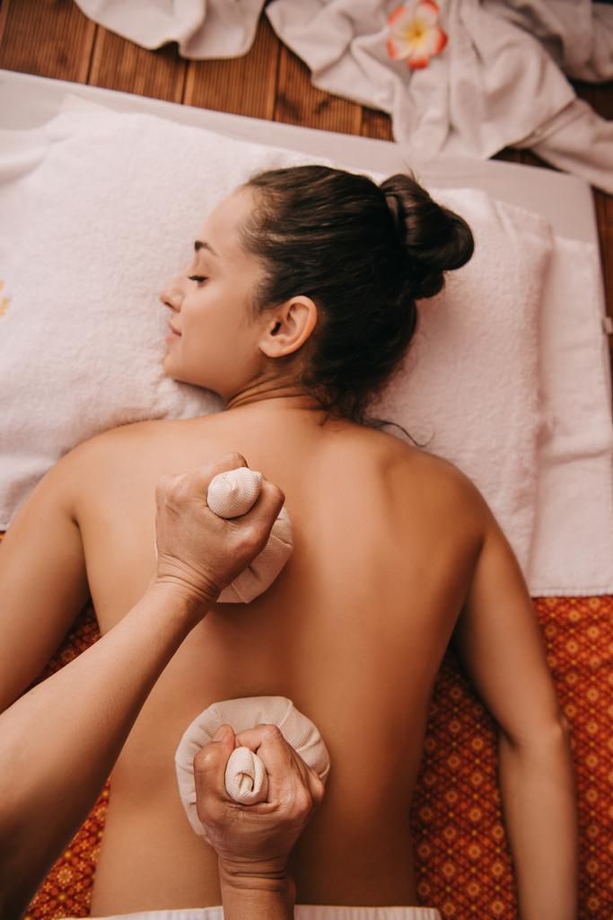 vista ritagliata di massaggiatore facendo massaggio alla schiena con le palle di erbe per la donna in spa
 - Foto, immagini