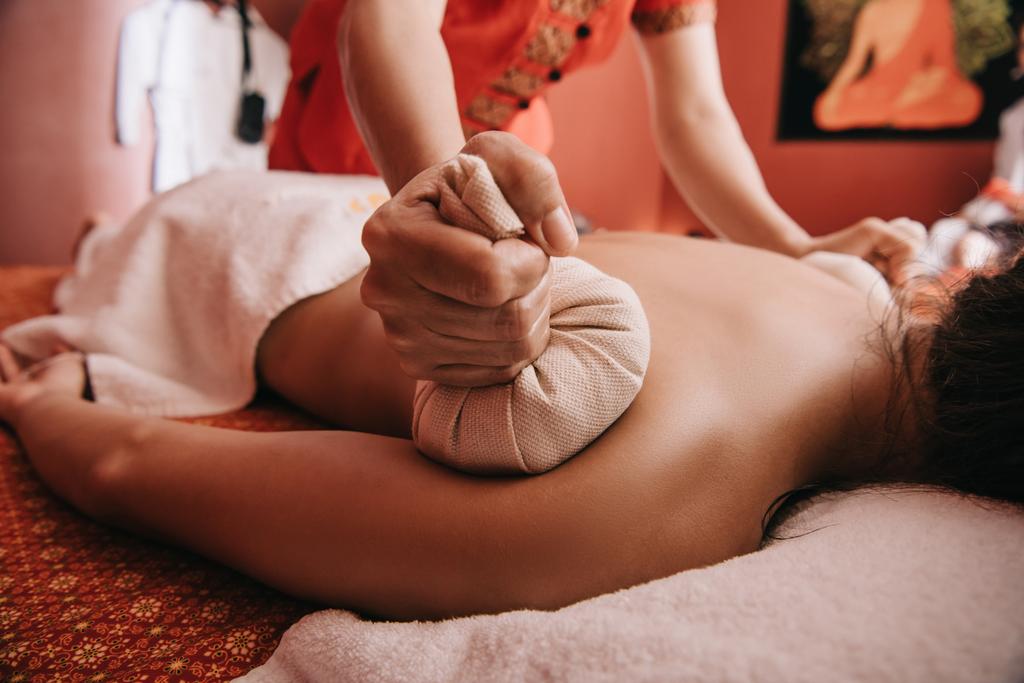 bijgesneden beeld van masseur doet terug massage met kruiden ballen naar vrouw in Spa - Foto, afbeelding