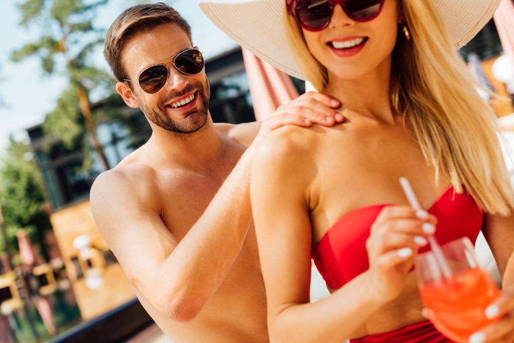 リゾートでガールフレンドのためのマッサージを行うサングラスで笑顔の男 - 写真・画像