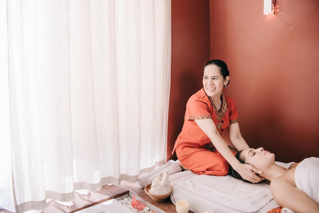 улыбающийся азиатский массажист делает массаж шеи женщине в спа-салоне
  - Фото, изображение