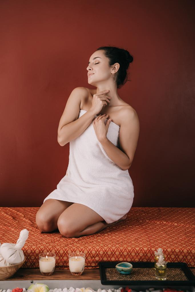 ελκυστική γυναίκα με κλειστά μάτια σε πετσέτα κάθεται στο χαλάκι μασάζ  - Φωτογραφία, εικόνα