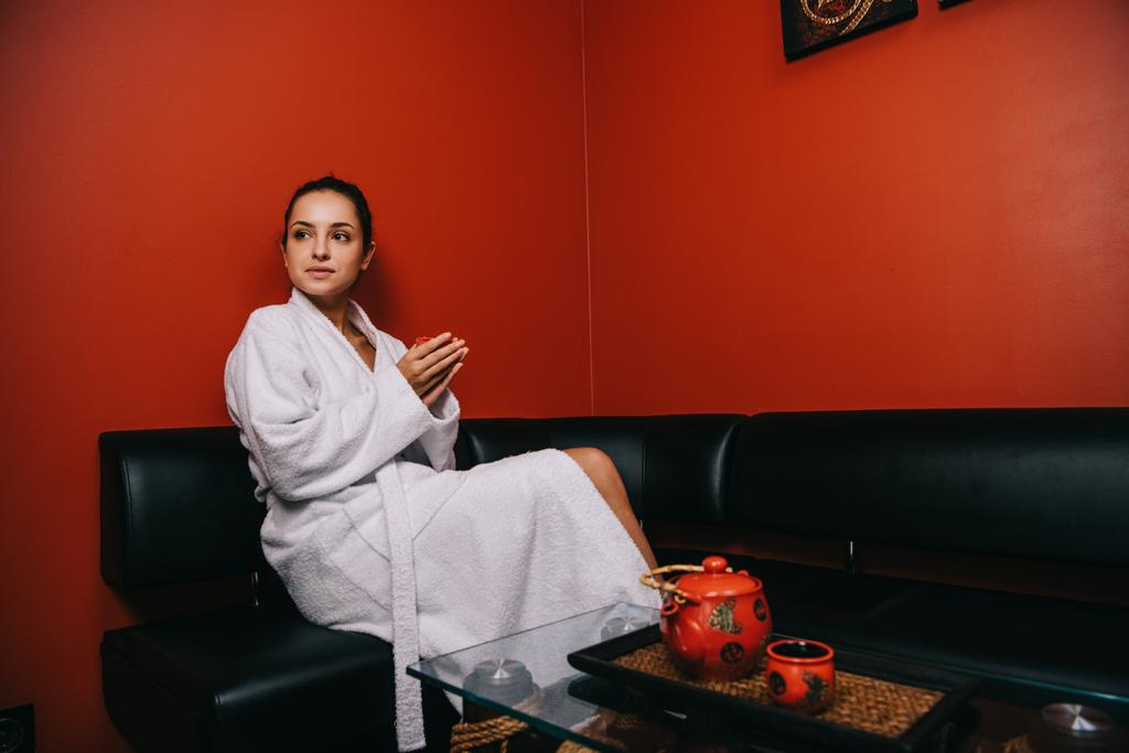 viehättävä nainen valkoisessa kylpytakissa istuu sohvalla ja pitää kuppi
  - Valokuva, kuva