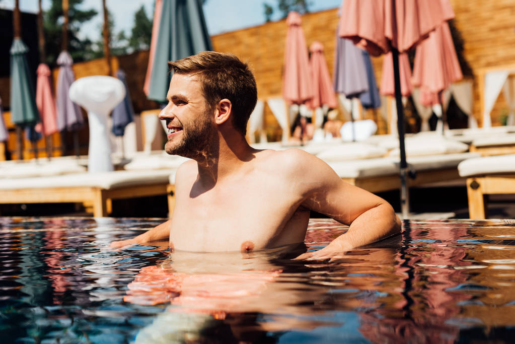 glücklicher junger Mann ohne Hemd im Schwimmbad bei sonnigem Tag - Foto, Bild