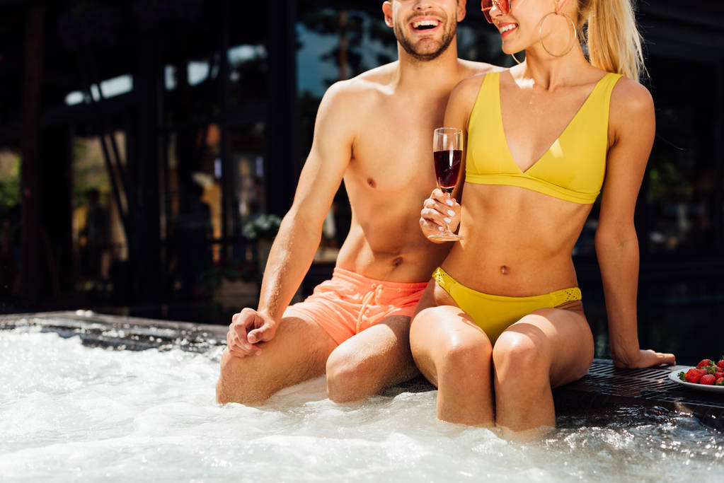 スイミングプールで赤ワインとイチゴとセクシーな笑顔のカップルのトリミングビュー - 写真・画像