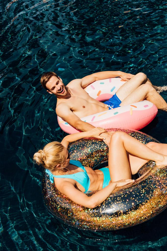 šťastný a bosný pár ležící na plaveckých kruzích v bazénu - Fotografie, Obrázek