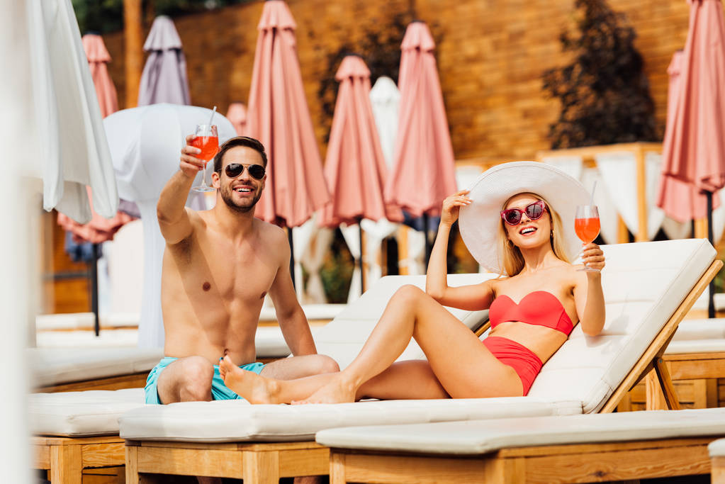 sexy couple holding glasses of cocktails at resort in sunny day - Photo, Image
