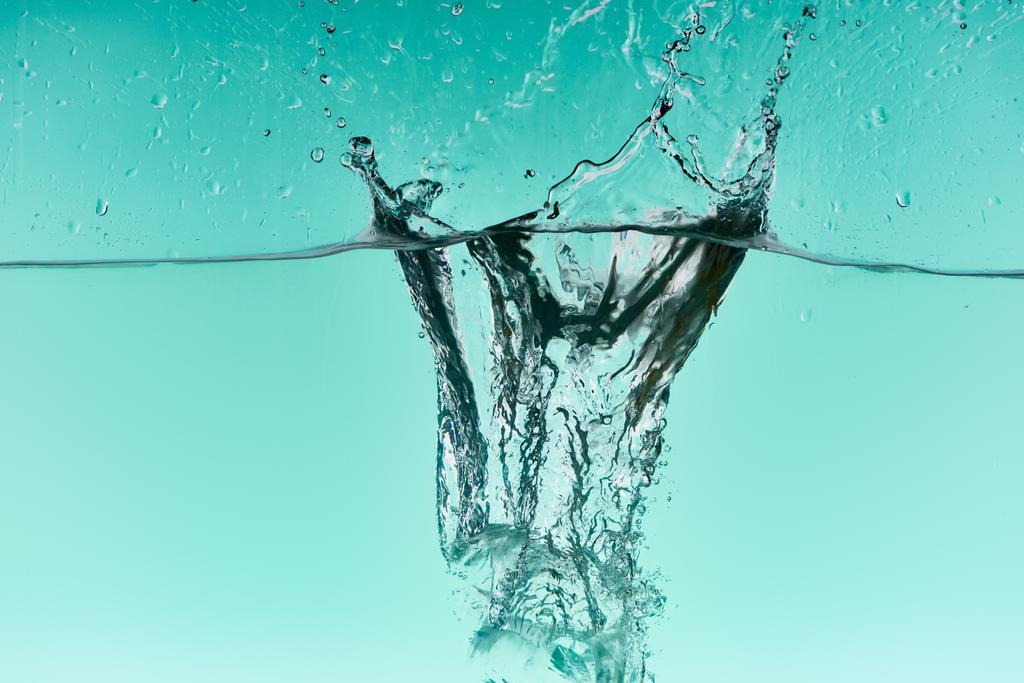 klare Eiswürfel fallen tief ins Wasser mit Spritzer auf türkisfarbenem Hintergrund - Foto, Bild