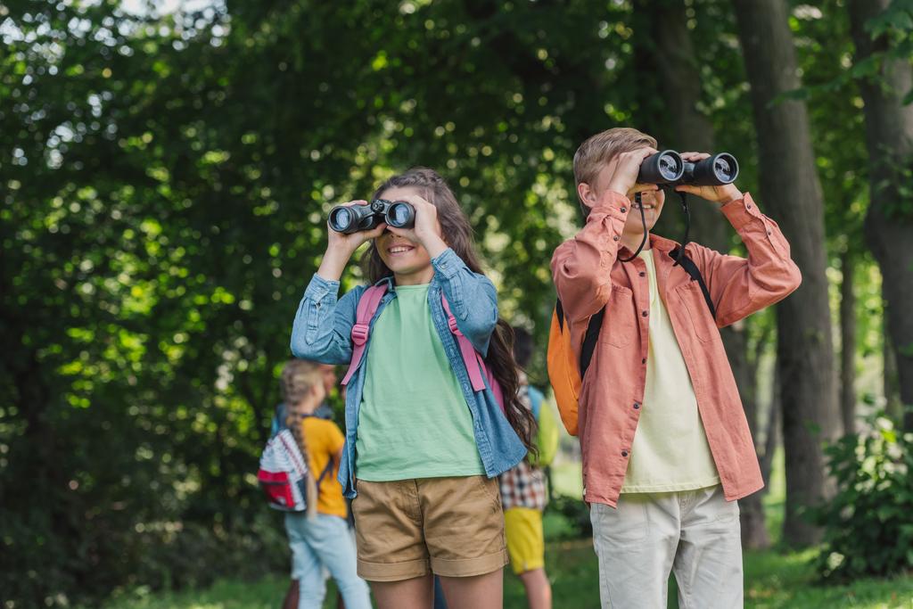 enfoque selectivo de niños alegres mirando a través de prismáticos en el parque
  - Foto, Imagen
