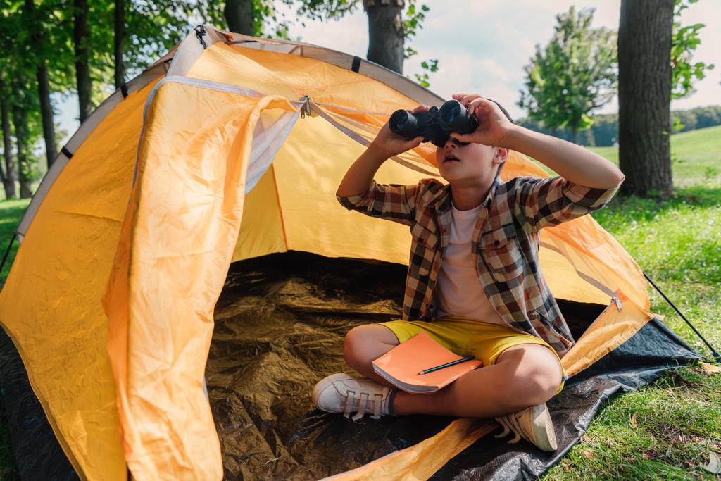 Yllättynyt lapsi katselee kiikarit leirissä
  - Valokuva, kuva