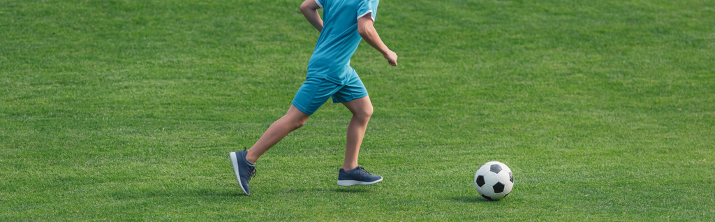 panoramic shit of kid in sportswear running on green grass with football  - Foto, afbeelding