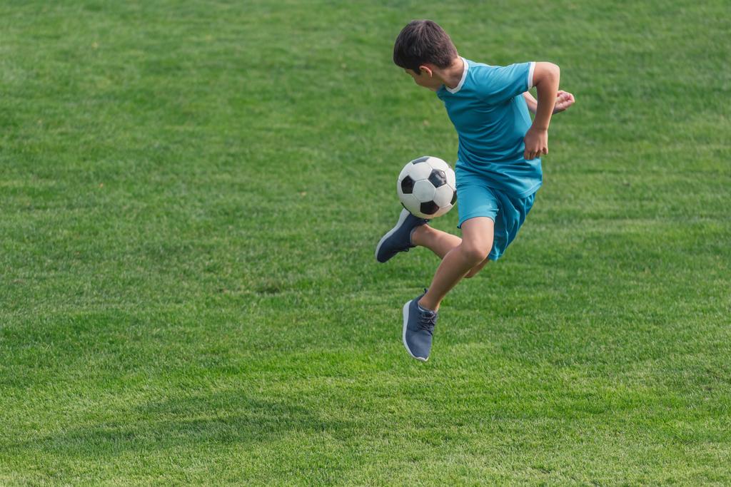 kid in sportswear jumping on green grass with football  - Photo, Image