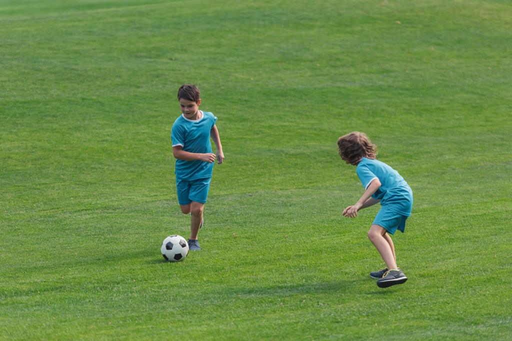 χαριτωμένα αγόρια σε αθλητικά είδη παίζοντας ποδόσφαιρο στο γρασίδι  - Φωτογραφία, εικόνα