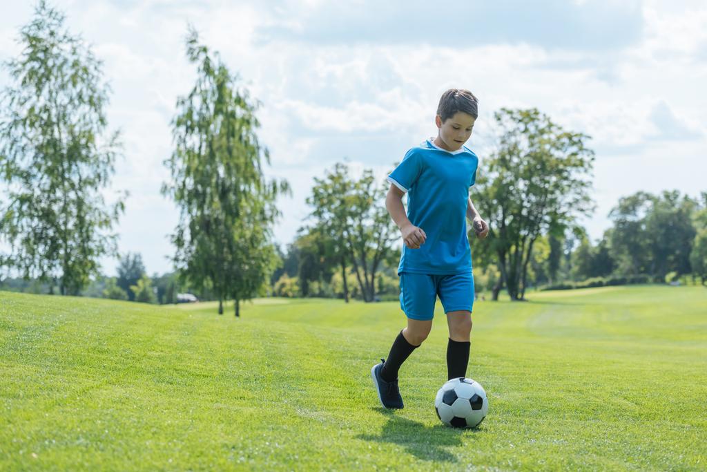 lindo niño en ropa deportiva corriendo sobre hierba verde con el fútbol
  - Foto, Imagen