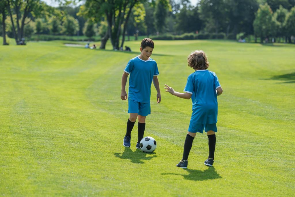 πίσω όψη του σγουρά αγόρι παίζοντας ποδόσφαιρο με το φίλο  - Φωτογραφία, εικόνα