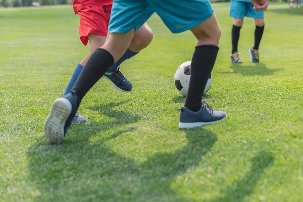 oříznutý pohled na kluky hrající fotbal na trávě  - Fotografie, Obrázek