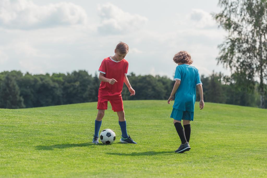 schattig krullend jongen voetbal spelen met vriend op gras  - Foto, afbeelding