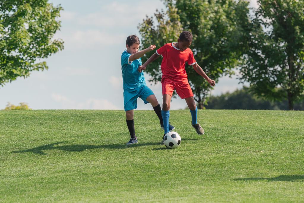 schattig multiculturele kinderen spelen voetbal op gras  - Foto, afbeelding