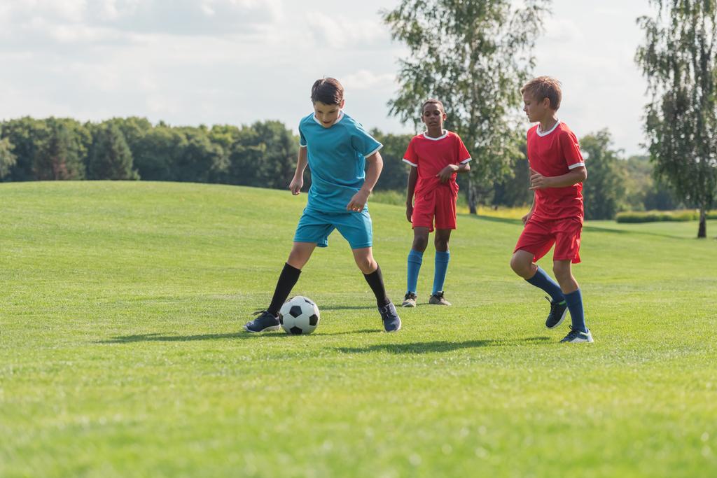 緑の草の上でサッカーをするかわいい多文化の友人  - 写真・画像