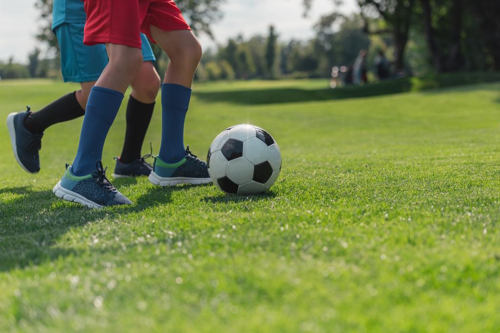 обрезанный вид детей, играющих в футбол на траве
  - Фото, изображение