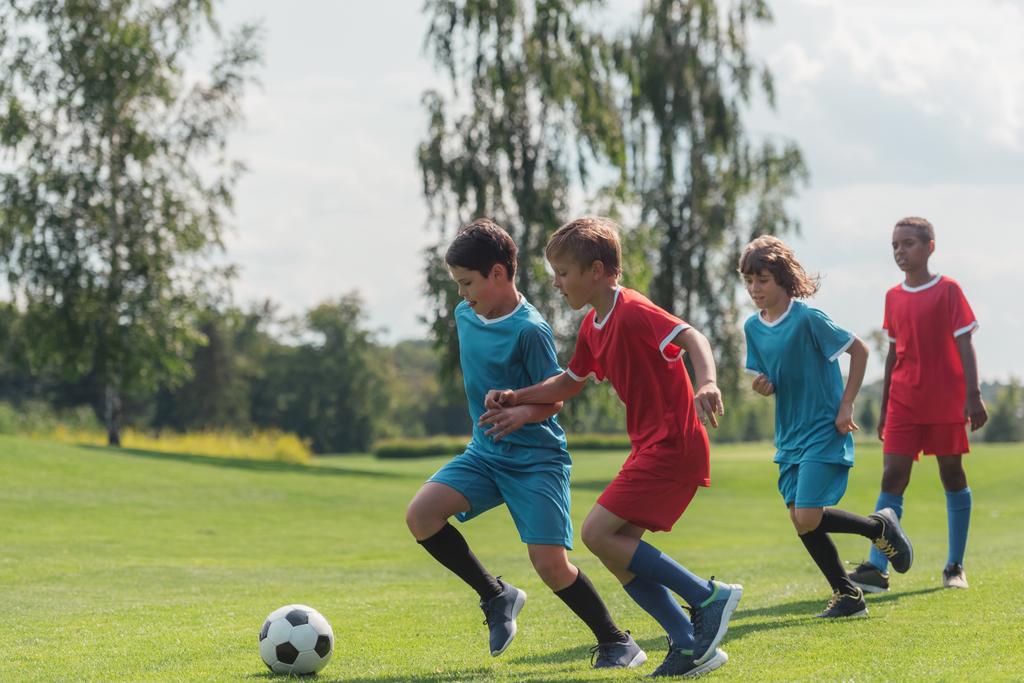 quatre enfants multiculturels jouant au football sur l'herbe
   - Photo, image