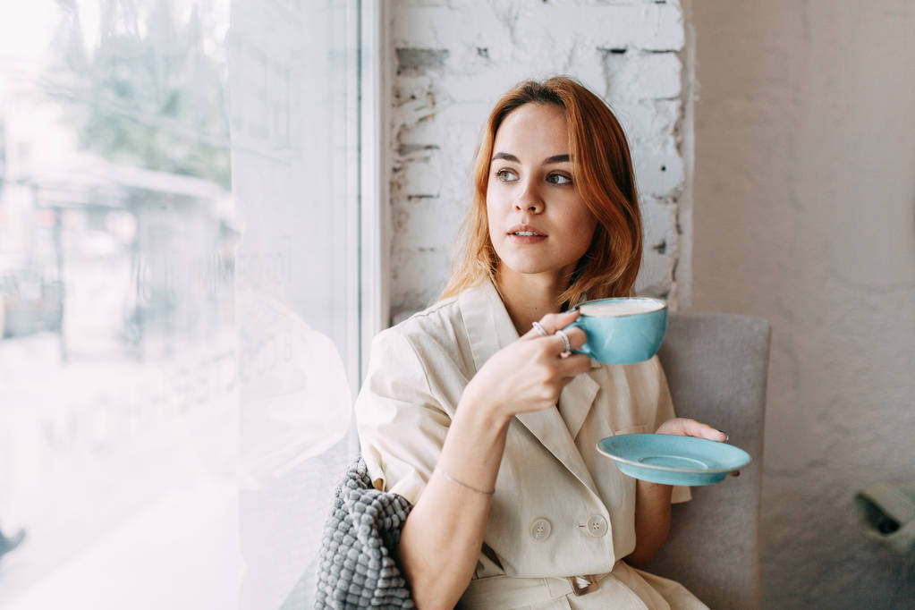  γυναίκα στη δουλειά σε ένα ελαφρύ καφενείο. νεαρό κορίτσι blogger με μια κούπα καφέ. - Φωτογραφία, εικόνα