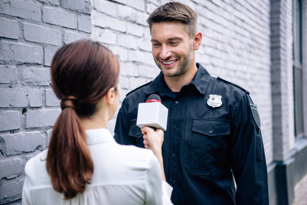 dziennikarz trzyma mikrofon i rozmawia z przystojnym policjantem w mundurze - Zdjęcie, obraz