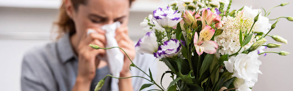 Panoramaaufnahme eines Blumenstraußes in der Nähe einer Frau mit Pollenallergie, die in Gewebe niest  - Foto, Bild