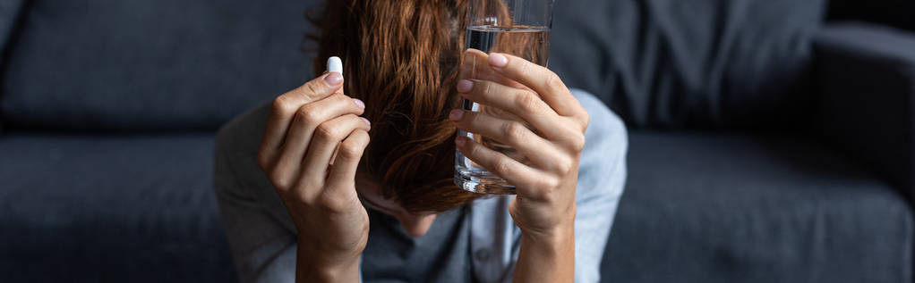 panoramische foto van zieke vrouw met pil en glas water thuis - Foto, afbeelding