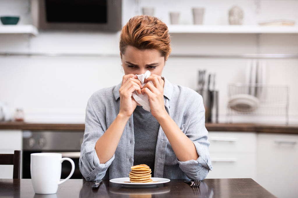 mujer enferma estornudando en servilleta cerca de sabrosos panqueques en casa
  - Foto, imagen
