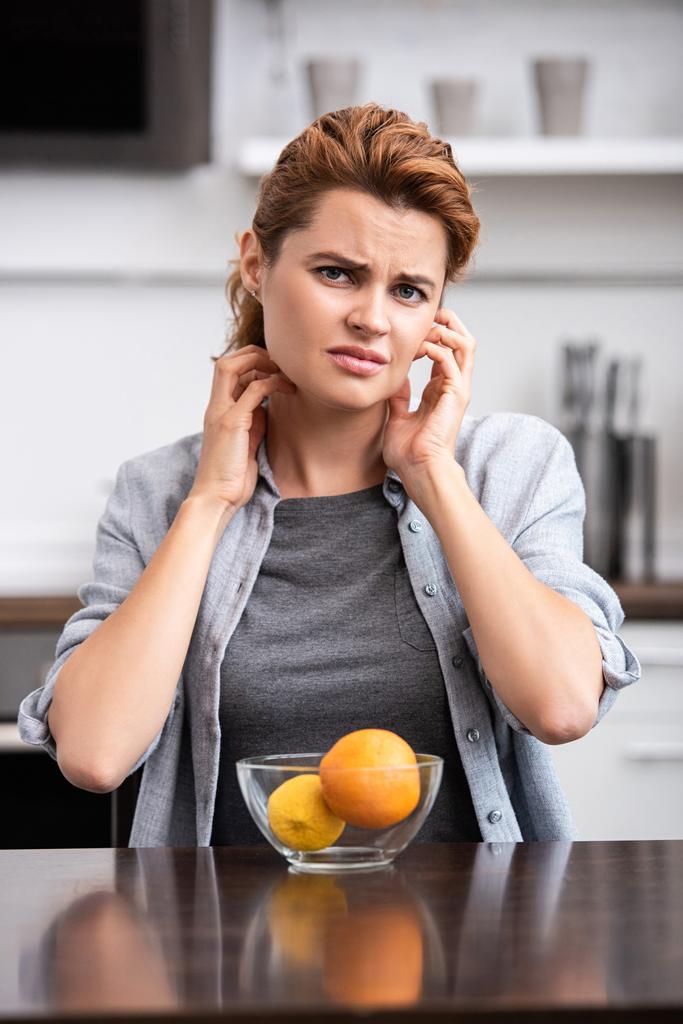 sad woman scratching neck near glass bowl with fruits  - Photo, Image