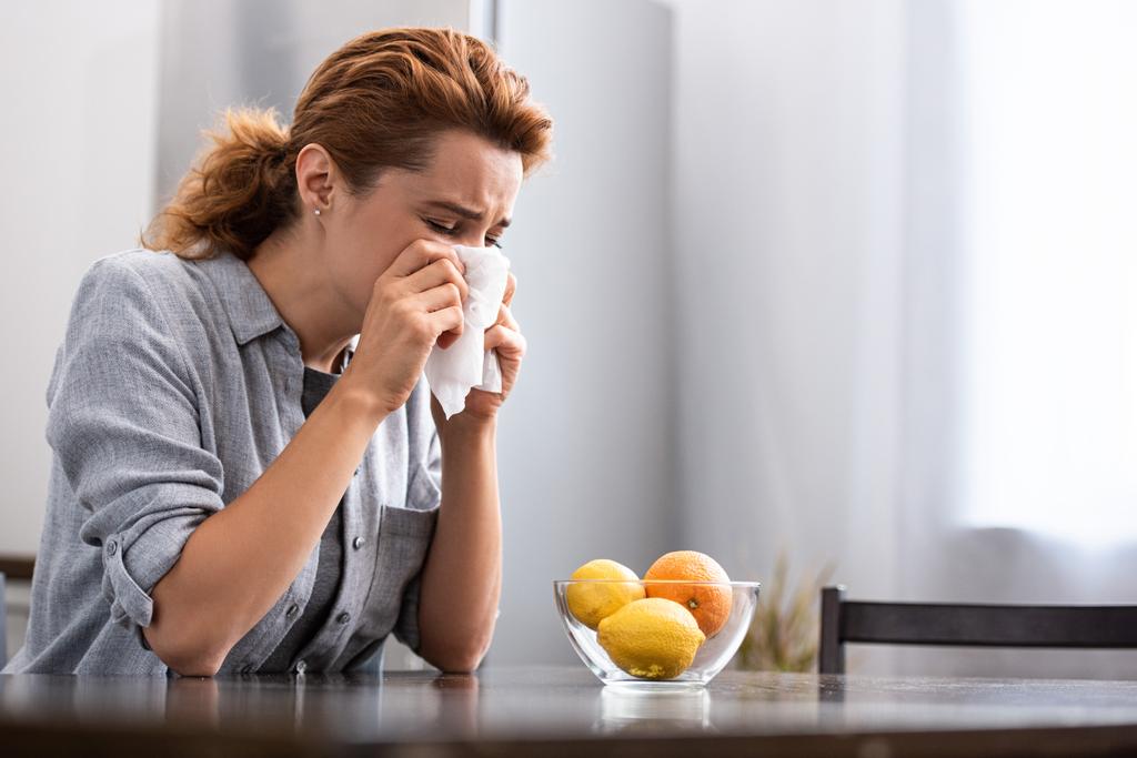 Frau mit laufende Nase niest in Gewebe in der Nähe von Orange und Zitronen in Schale  - Foto, Bild