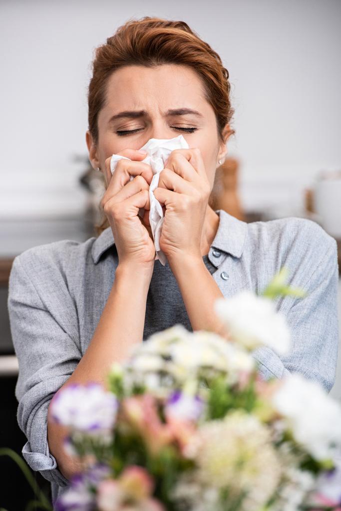 selective focus of woman with pollen allergy sneezing in tissue near flowers  - Photo, Image