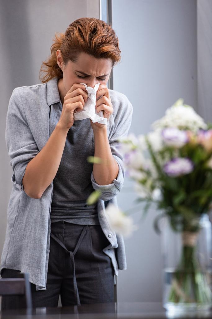 enfoque selectivo de la mujer estornudando en tejido cerca de flores en jarrón
  - Foto, Imagen